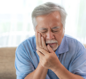 Homem com expressão de dor segurando a lateral do rosto, aparente desconforto devido a dor de dente. Cena ilustrativa de problemas odontológicos, como cáries ou sensibilidade dentária. Possíveis problemas que levam a procura do agendamento ou do sistema dentista 24 horas para atendimento de urgência e emergência.